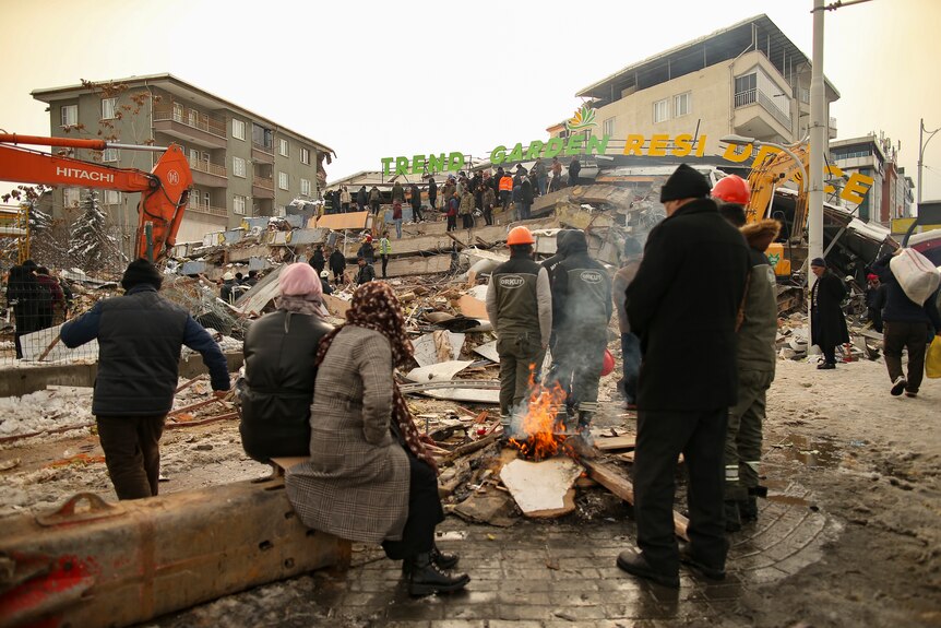 A crowd of people gathered in a street look at a collapsed building