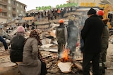 A crowd of people gathered in a street look at a collapsed building