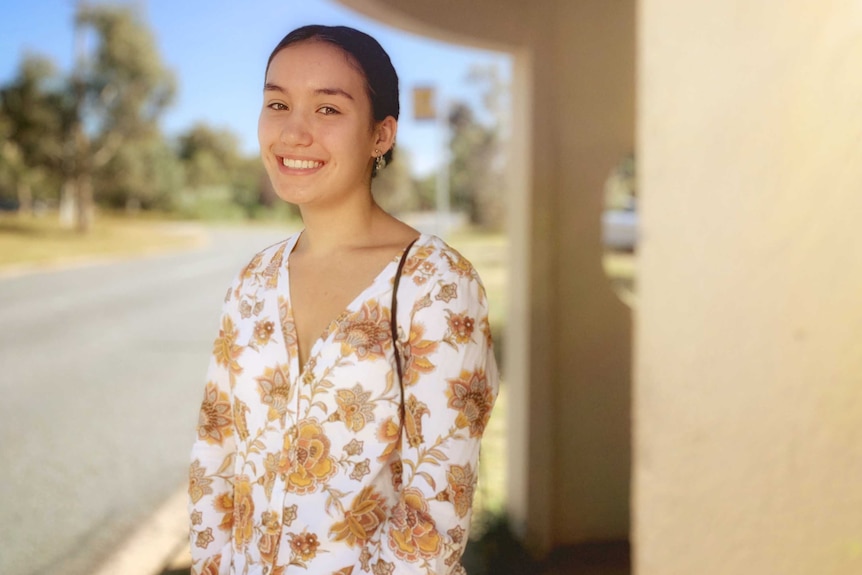 Hannah smiles, standing at a Canberra bus stop.