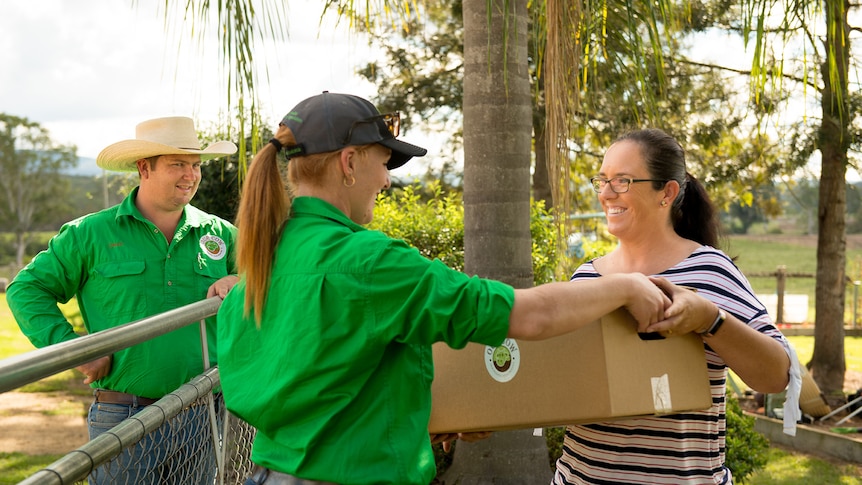 A woman in  green shirt hands another woman a box of meat.