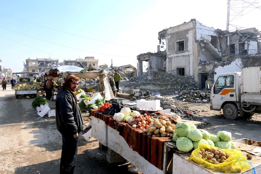 A man looks at a market stall surround by rubble