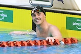 A man in a black swimming cap smiles from the end of a pool