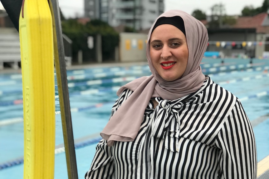 Une femme portant un hijab debout près d'une piscine.