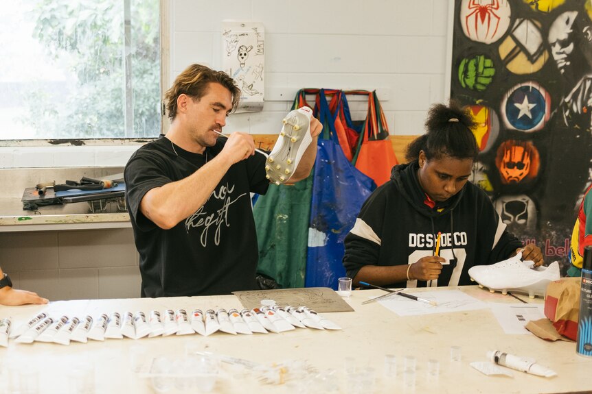 A man and a girl paint football boots with Indigenous designs