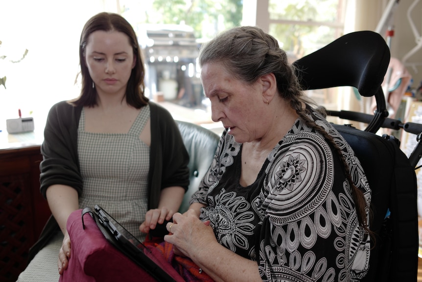 A woman in a wheelchair sits with a younger woman looking at a screen