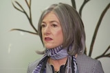 A woman with grey hair wearing a checked jacket and a purple scarf