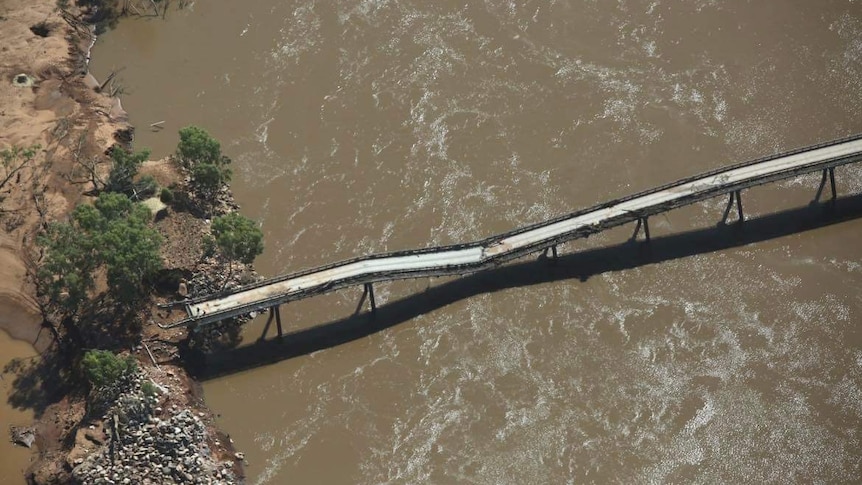 A bridge over brown river water that is sagging in the middle. 