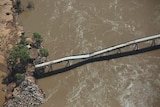 A bridge over brown river water that is sagging in the middle. 