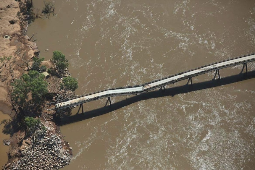 A bridge over brown river water that is sagging in the middle. 