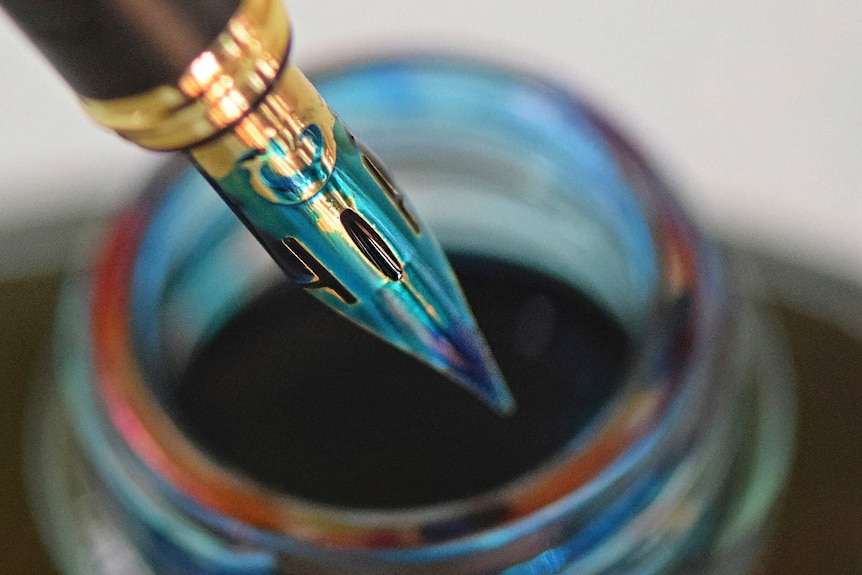 A fountain pen with a flex nib dips into a pot of turquoise ink.