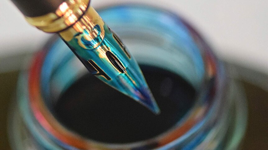 A fountain pen with a flex nib dips into a pot of turquoise ink.