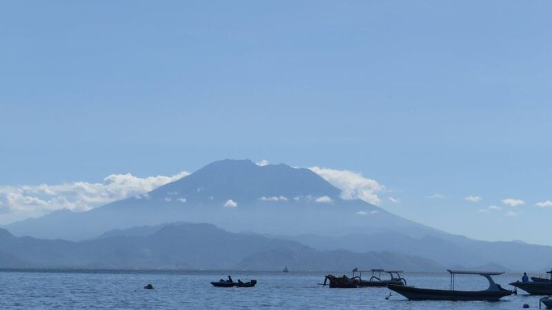 Mount Agung is seen in the distance with boats in a bay in the foreground.