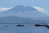 Mount Agung is seen in the distance with boats in a bay in the foreground.