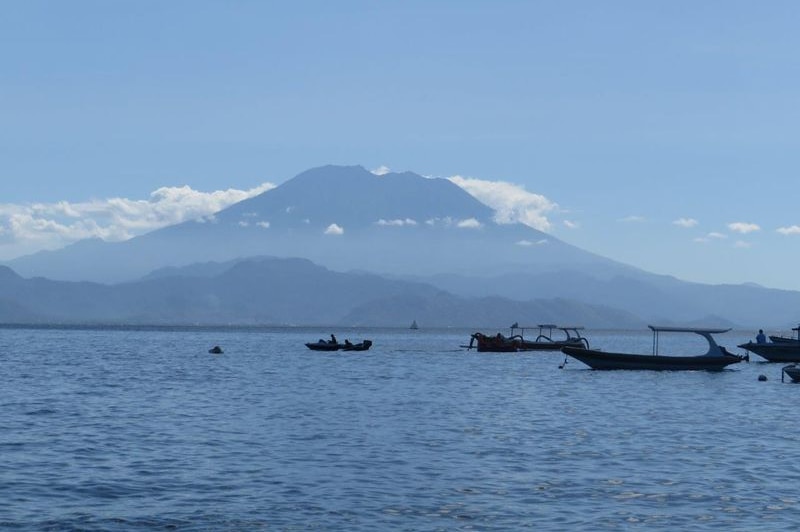 Mount Agung is seen in the distance with boats in a bay in the foreground.