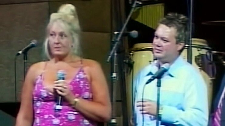 Nicola Gobbo on stage holding a microphone next to Carl Williams.