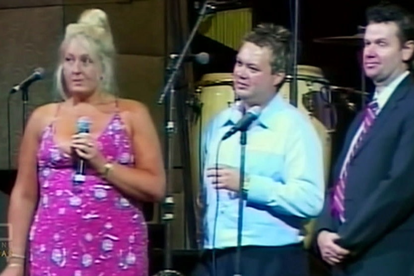Nicola Gobbo on stage holding a microphone next to Carl Williams.