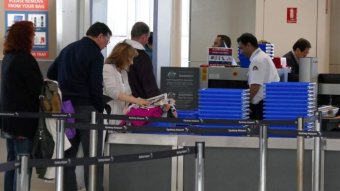People line up at an airport security checkpoint, having their bags run through scanners.