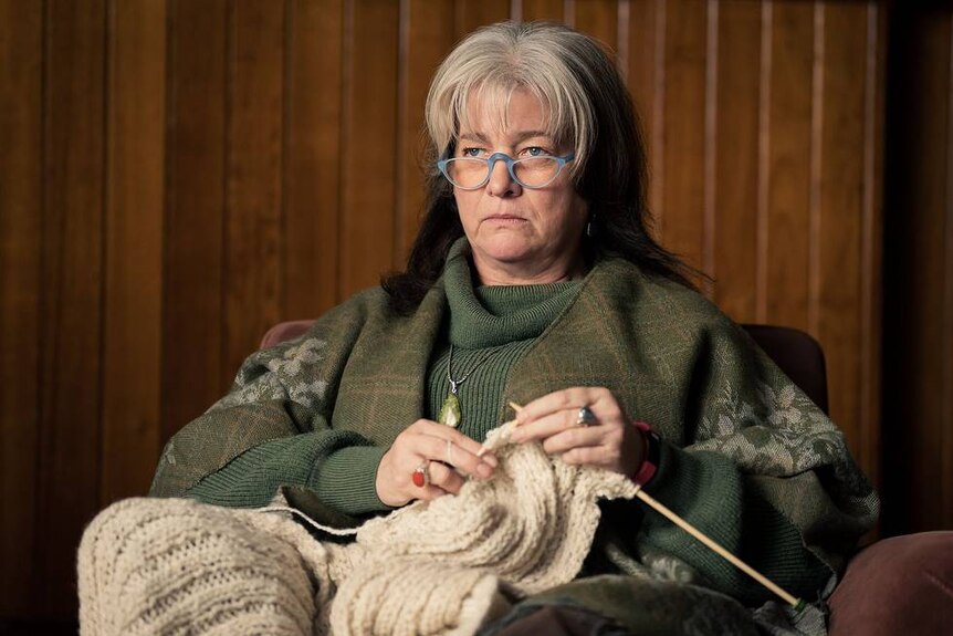 A woman is stitting down knitting.