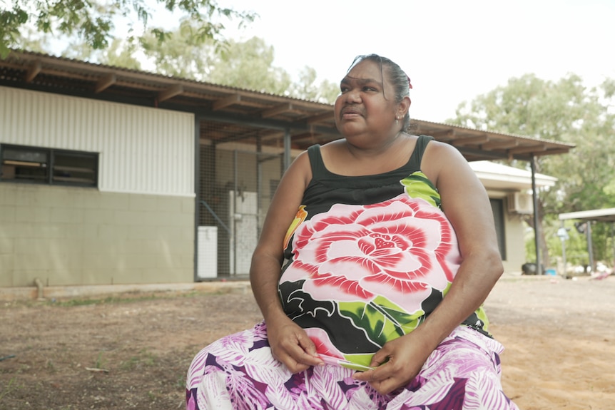 A woman in a dress sitting on a chair, outside a house in a remote community. 