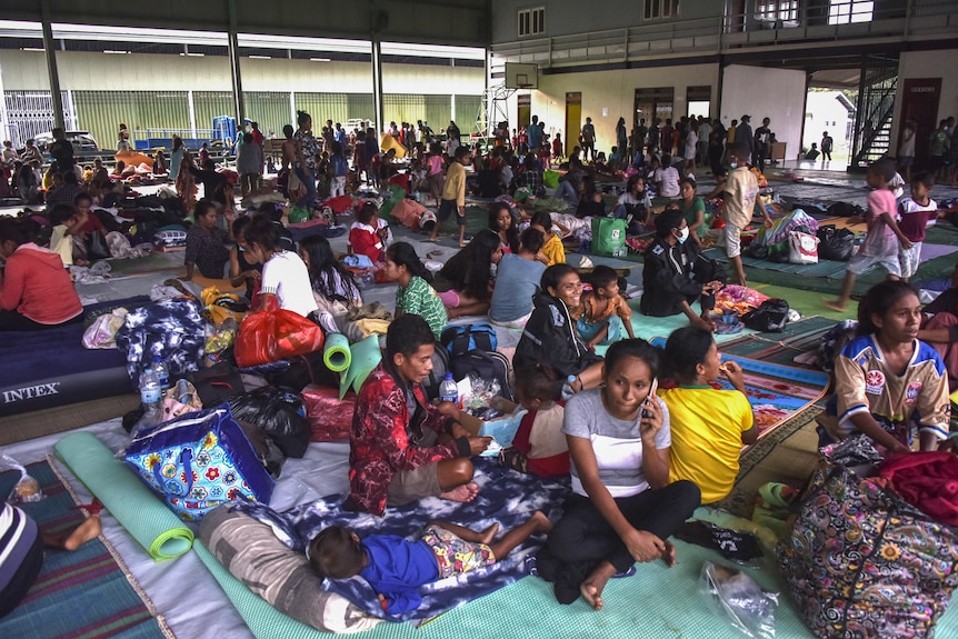 People sit on mats on the floor of an open space that is part of an emergency shelter.