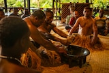 Photo of multiple men in ritual clothing making a drink out of roots.