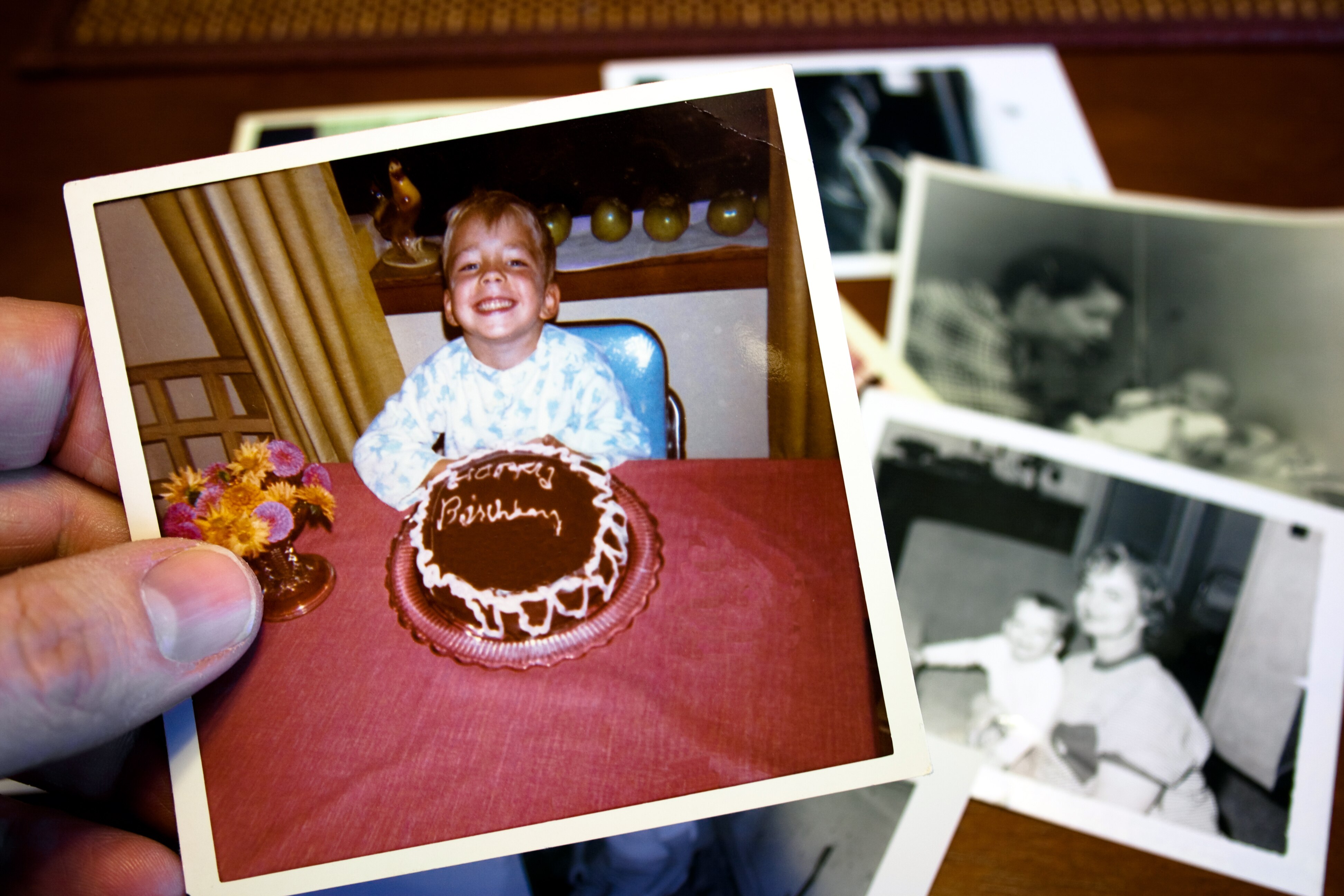 Image of a hand holding an old printed photo of a child sitting at a table with a birthday cake.