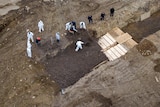 A drone shot of men in protective gear digging mass graves