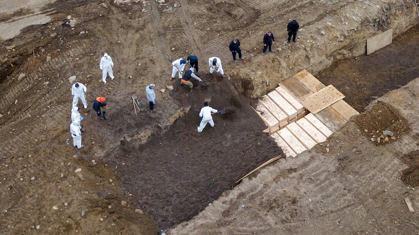 A drone shot of men in protective gear digging mass graves