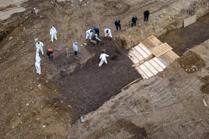 A drone shot of men in protective gear digging mass graves