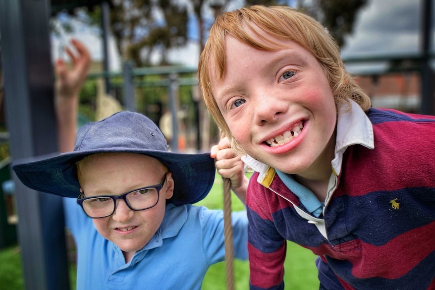 A picture of two boys smiling at the camera, with a school playground blurred in the background.