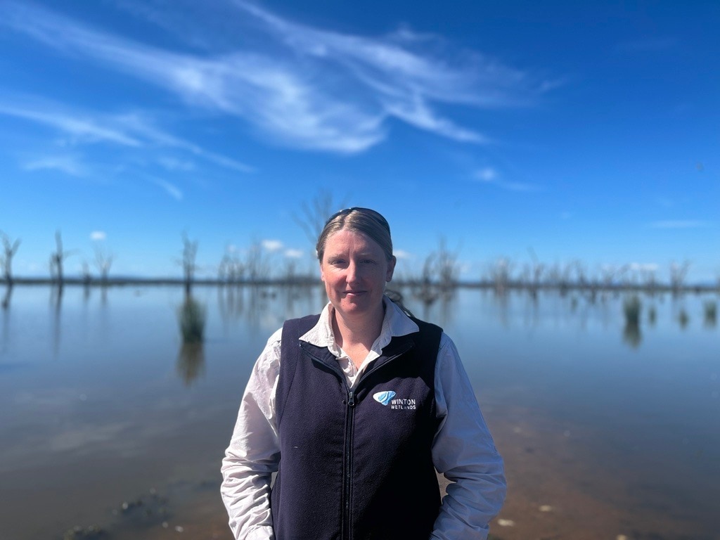 woman smiles at camera in front of wetland lanscape.