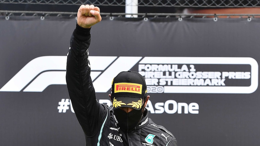 Lewis Hamilton stands with his right fist clenched and raised with his head down