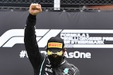 Lewis Hamilton stands with his right fist clenched and raised with his head down