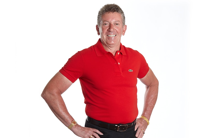 Mean wearing red polo shirt with man pants smiles, with hands on hips, in front of white backdrop.
