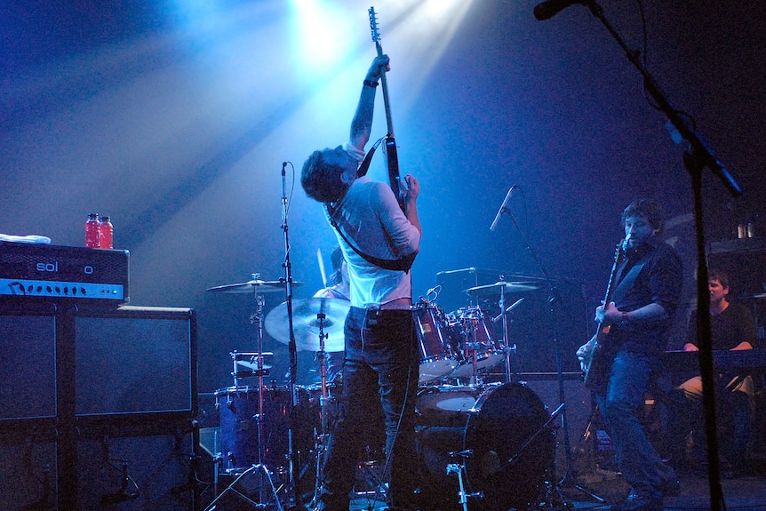 Blue lights highlight guitarist on stage lifting instrument up to ceiling