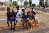 A group of six kids pose for the camera with their dog
