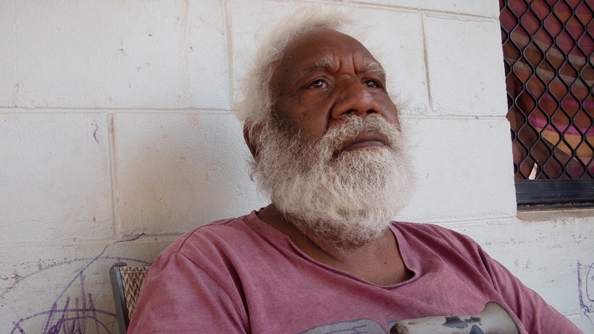 An older Aboriginal man looking pensive and holding a walking stick