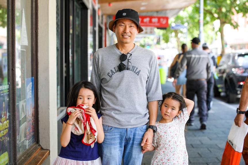 A man standing with two little girls in a street