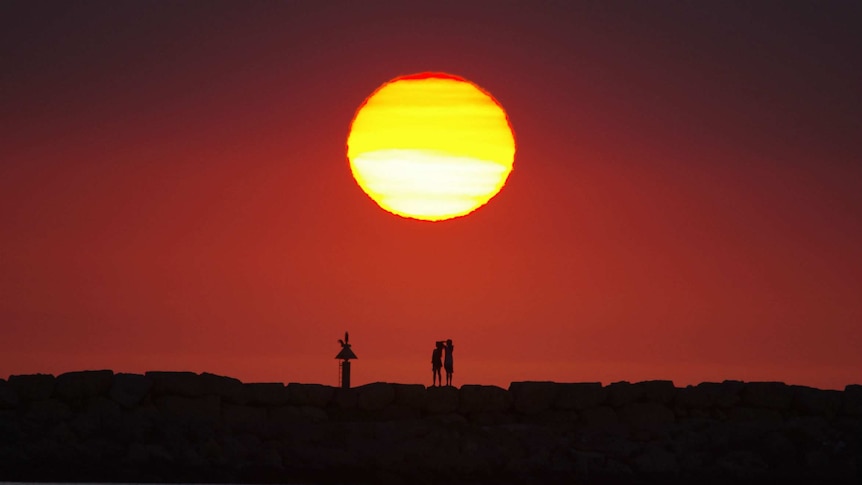 Two people in silhouette watching sunset from rocks