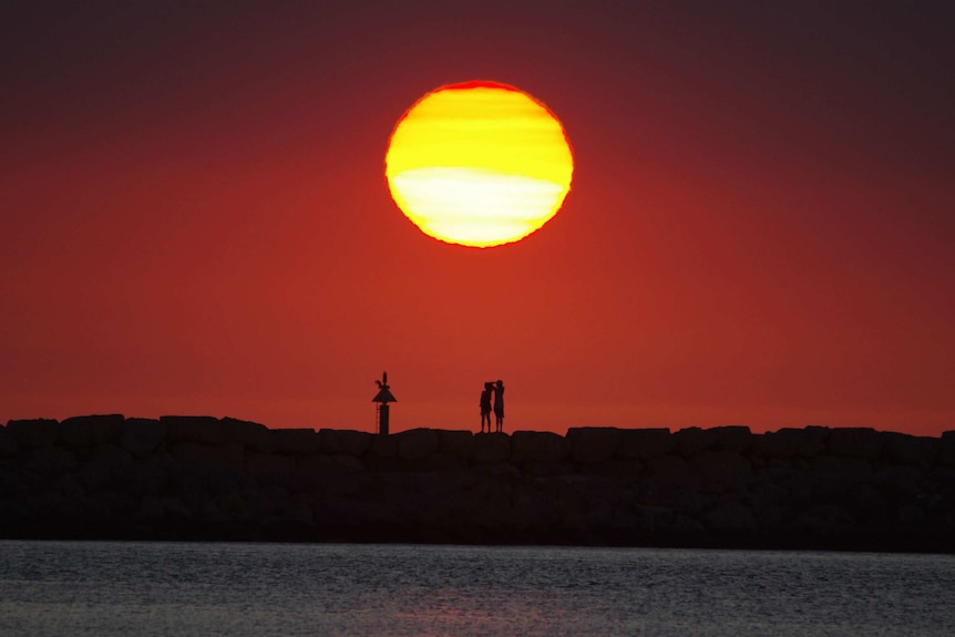 Two people in silhouette watching a sunset from rocks.