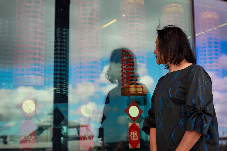 A Chinese woman looks at her art installation through the glass wall outside the Docklands library.