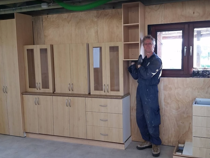 A man stands next to a wall of kitchen cabinets inside a shed