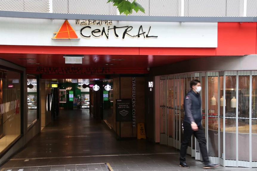 A man in a face mask walks past a closed shop at Melbourne Central.