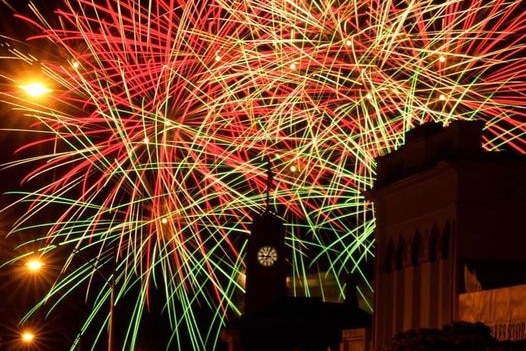 Long exposure image of green, yellow and red fireworks behind the silhouette of a city clock