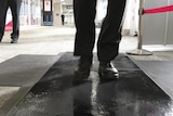 A person in black leather shoes walks over a wet black mat. 