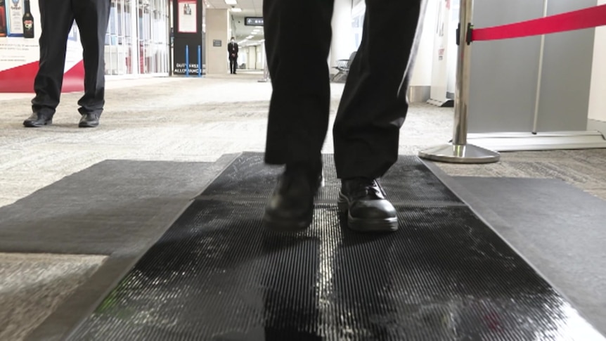 A person in black leather shoes walks over a wet black mat. 