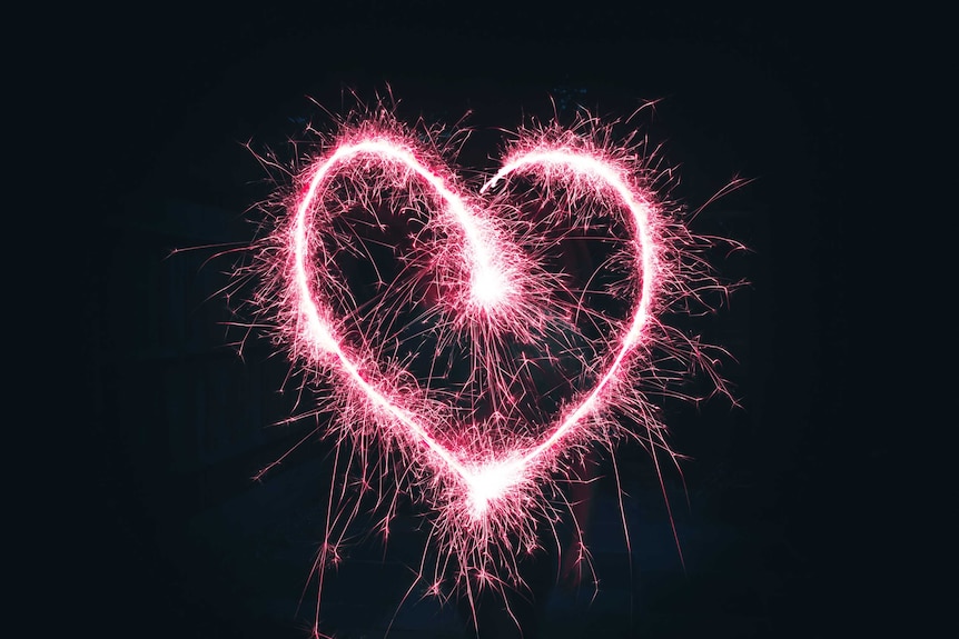 Pink sparkler in the dark drawing a love heart, representing the intensity of the initial stages of a romantic relationship.