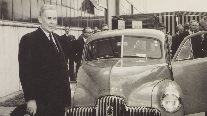 A black and white postcard of Ben Chifley standing in front of a Holden car.