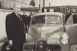 A black and white postcard of Ben Chifley standing in front of a Holden car.