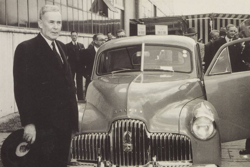 A black and white postcard of Ben Chifley standing in front of a Holden car.